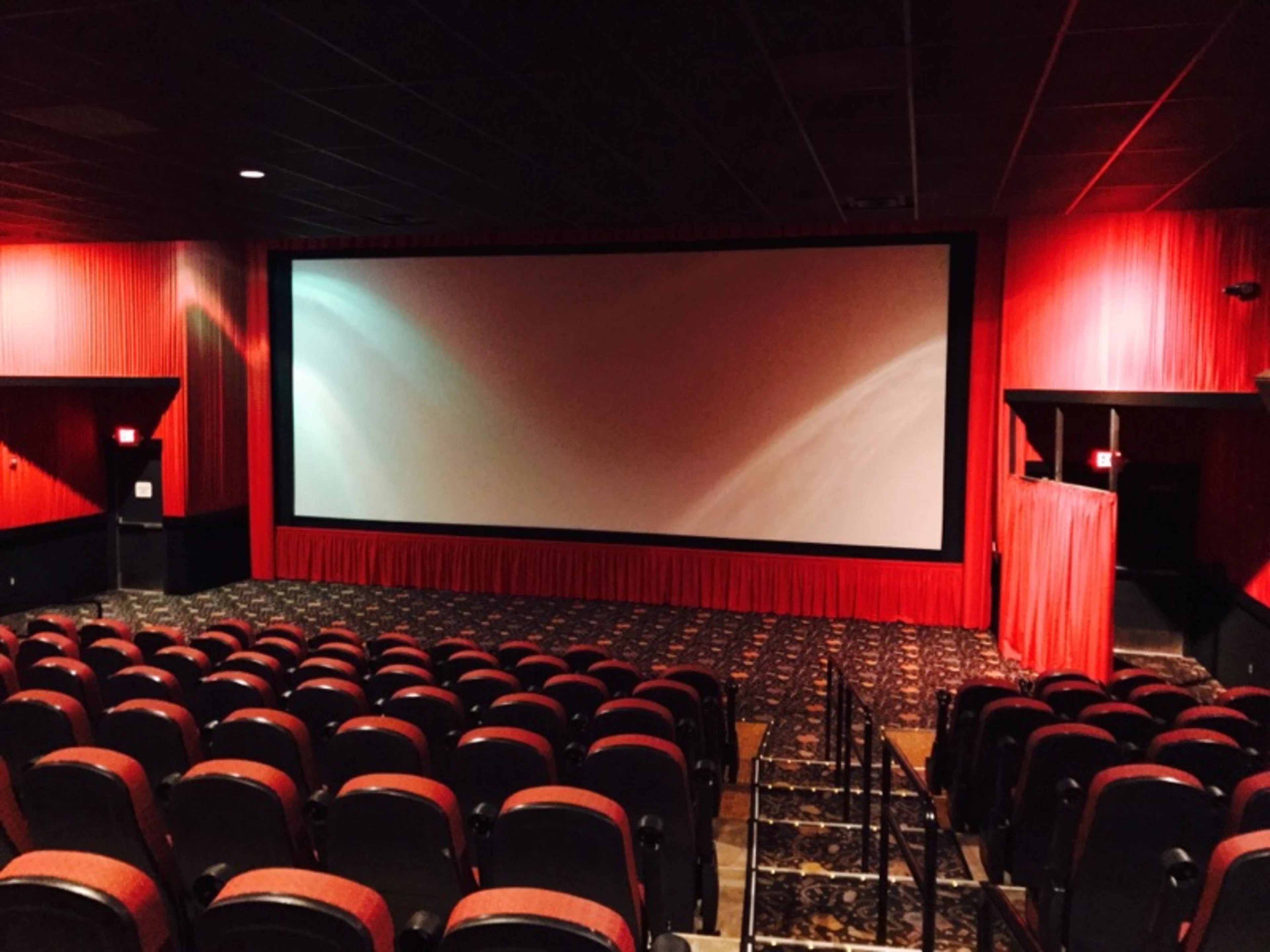 A conventional movie theater with red seats, red walls, and a large cinema screen.
