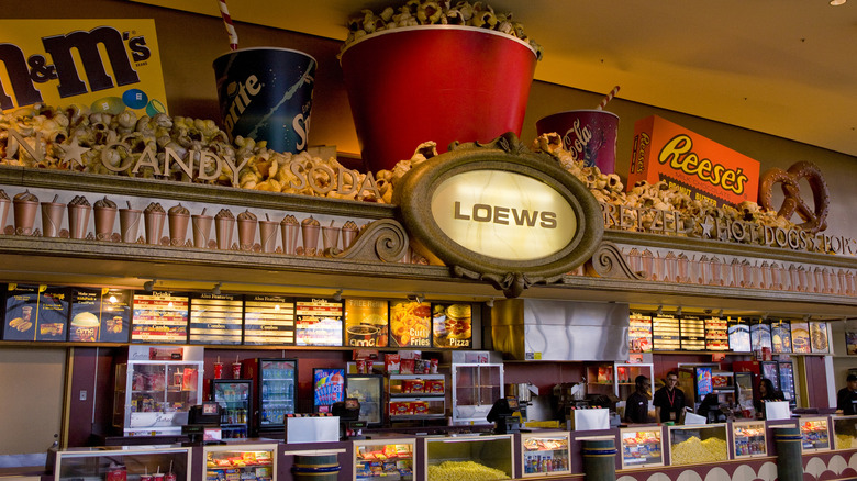 A brightly decorated movie-theater concession stand filled with popcorn, drinks, candy, and illuminated menu boards.
