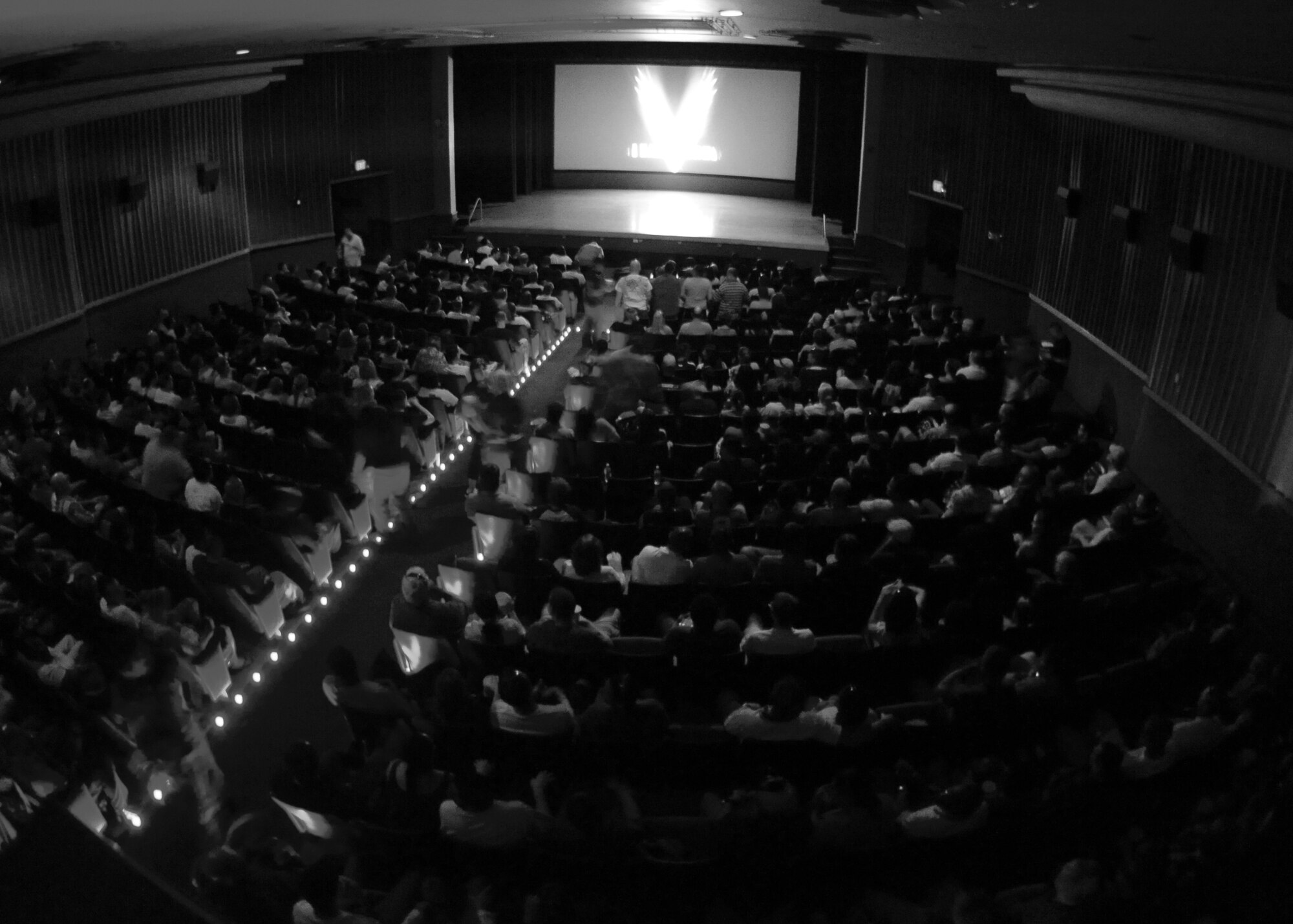 A crowded movie theater viewed from the back as an audience waits for a screening to begin.