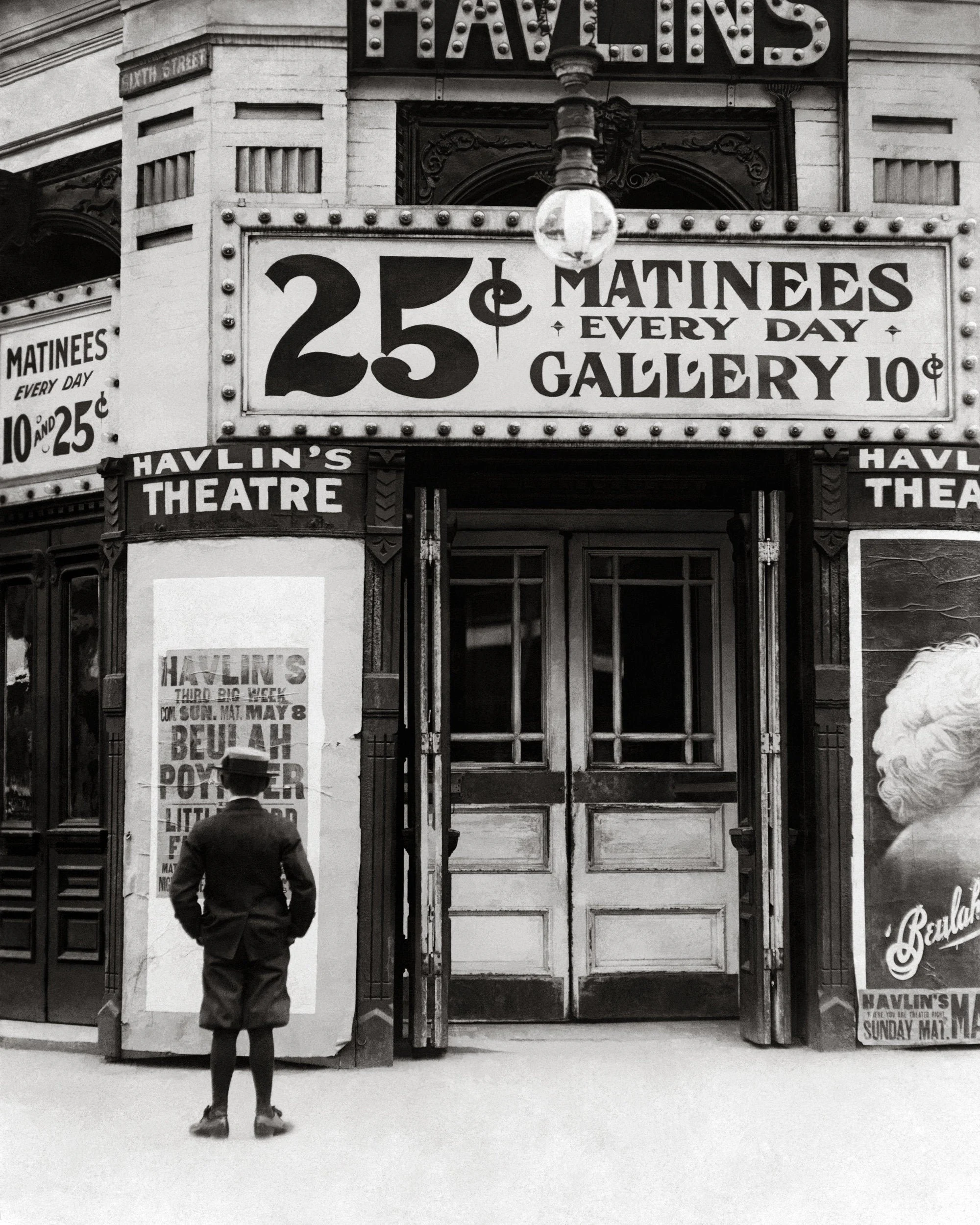 A historic black-and-white theater entrance advertising 25-cent matinees and 10-cent gallery tickets.