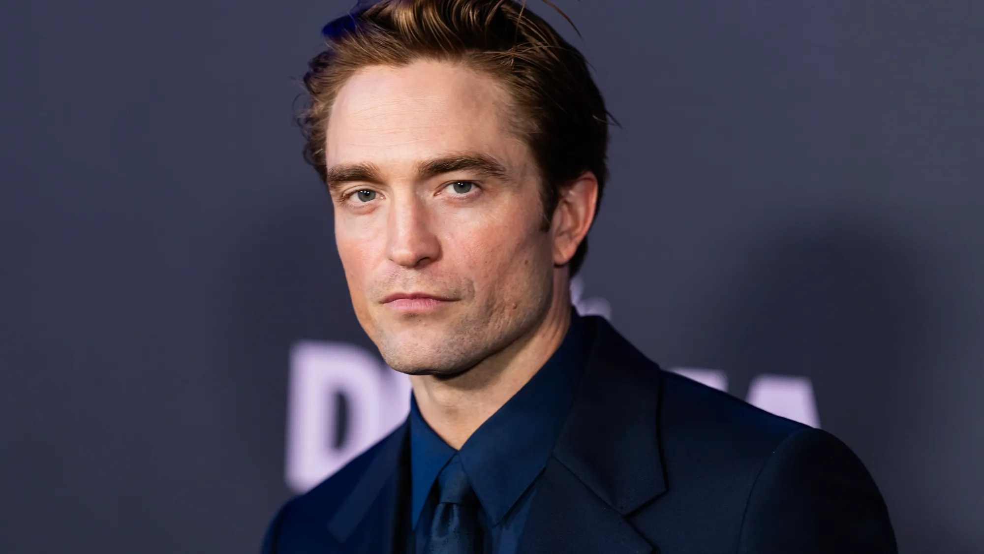 Robert Pattinson poses at a recent film event in a dark navy suit.