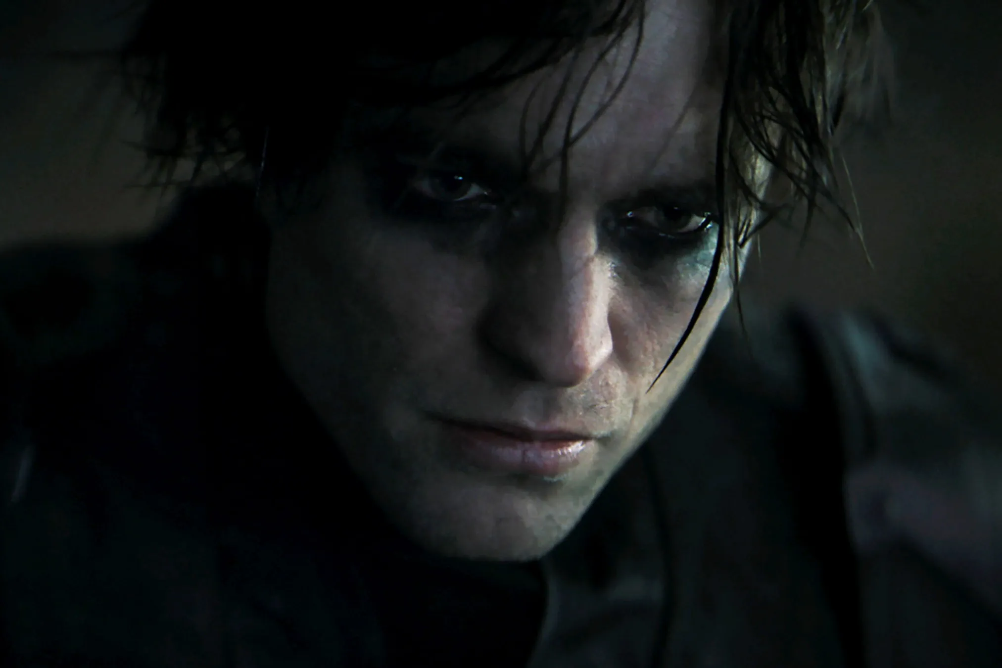 Robert Pattinson as Bruce Wayne looks forward with dark eye makeup around his eyes.