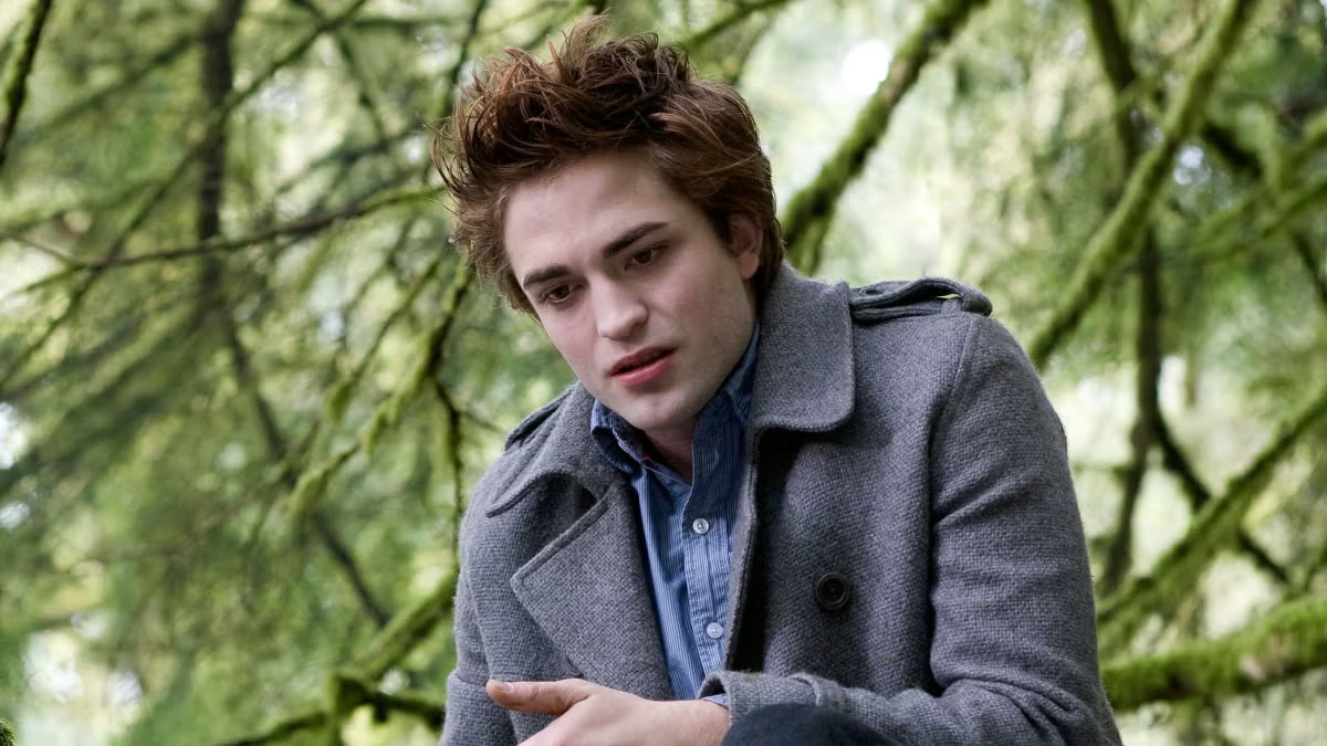 Robert Pattinson as Edward Cullen stands outdoors in a wooded setting.
