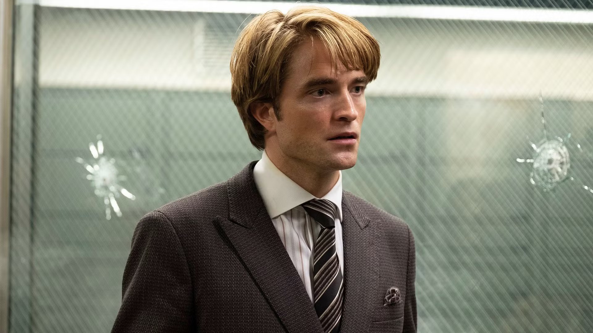 Robert Pattinson in a suit stands before cracked glass in Primetime.