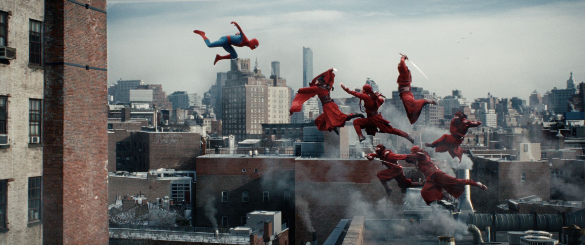 Spider-Man leaps across a New York rooftop while a group of red-clad fighters jump through the air behind him.