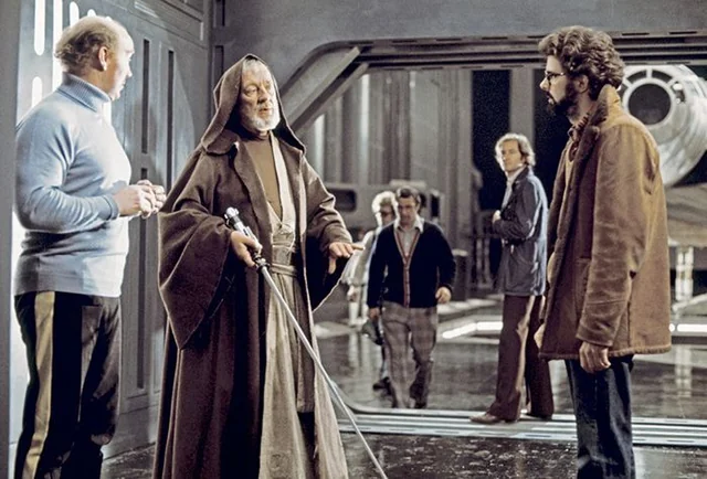 George Lucas stands on the Death Star set with Alec Guinness and members of the Star Wars production crew.