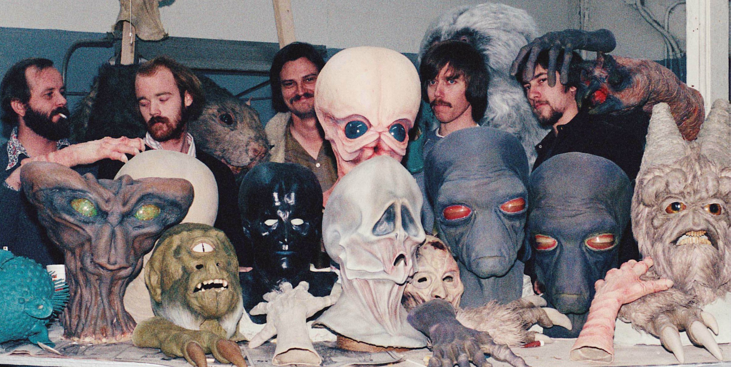 Creature artists pose behind an assortment of alien masks and prosthetics created for the Mos Eisley cantina.