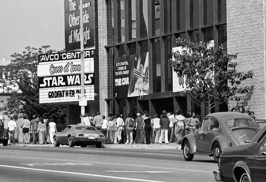 Moviegoers line up outside a theater with Star Wars displayed on the marquee during the film’s original theatrical era.