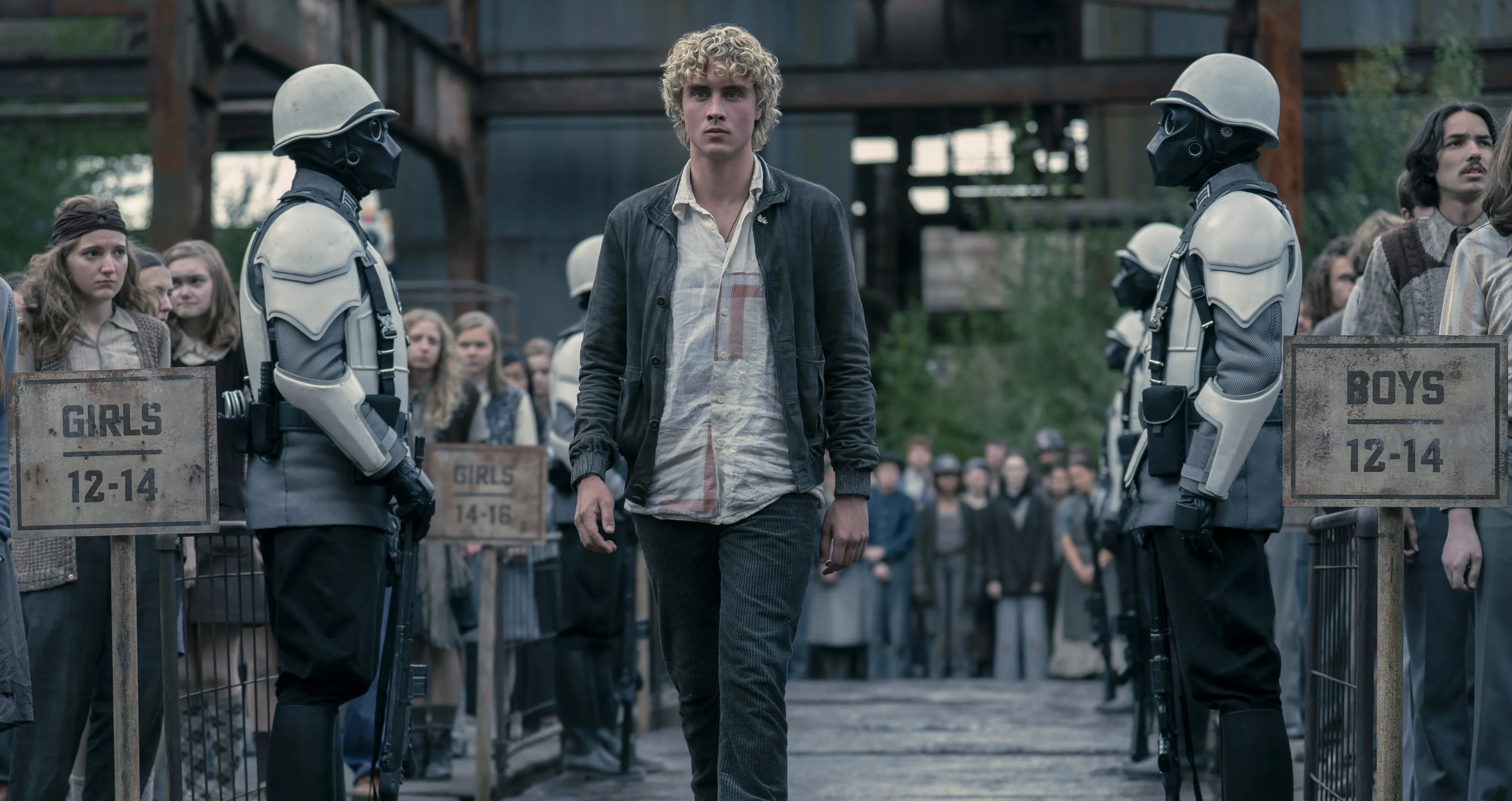 A young Haymitch Abernathy walks between armed Peacekeepers during a reaping in The Hunger Games: Sunrise on the Reaping.