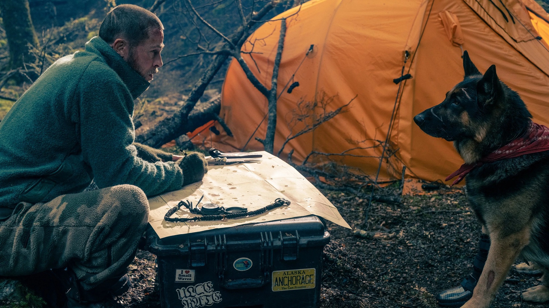 Brad Pitt studies a map across from a German shepherd beside an orange tent in Heart of the Beast.