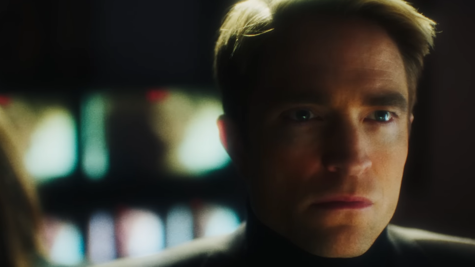 Robert Pattinson looks toward a bank of glowing television monitors in Primetime.