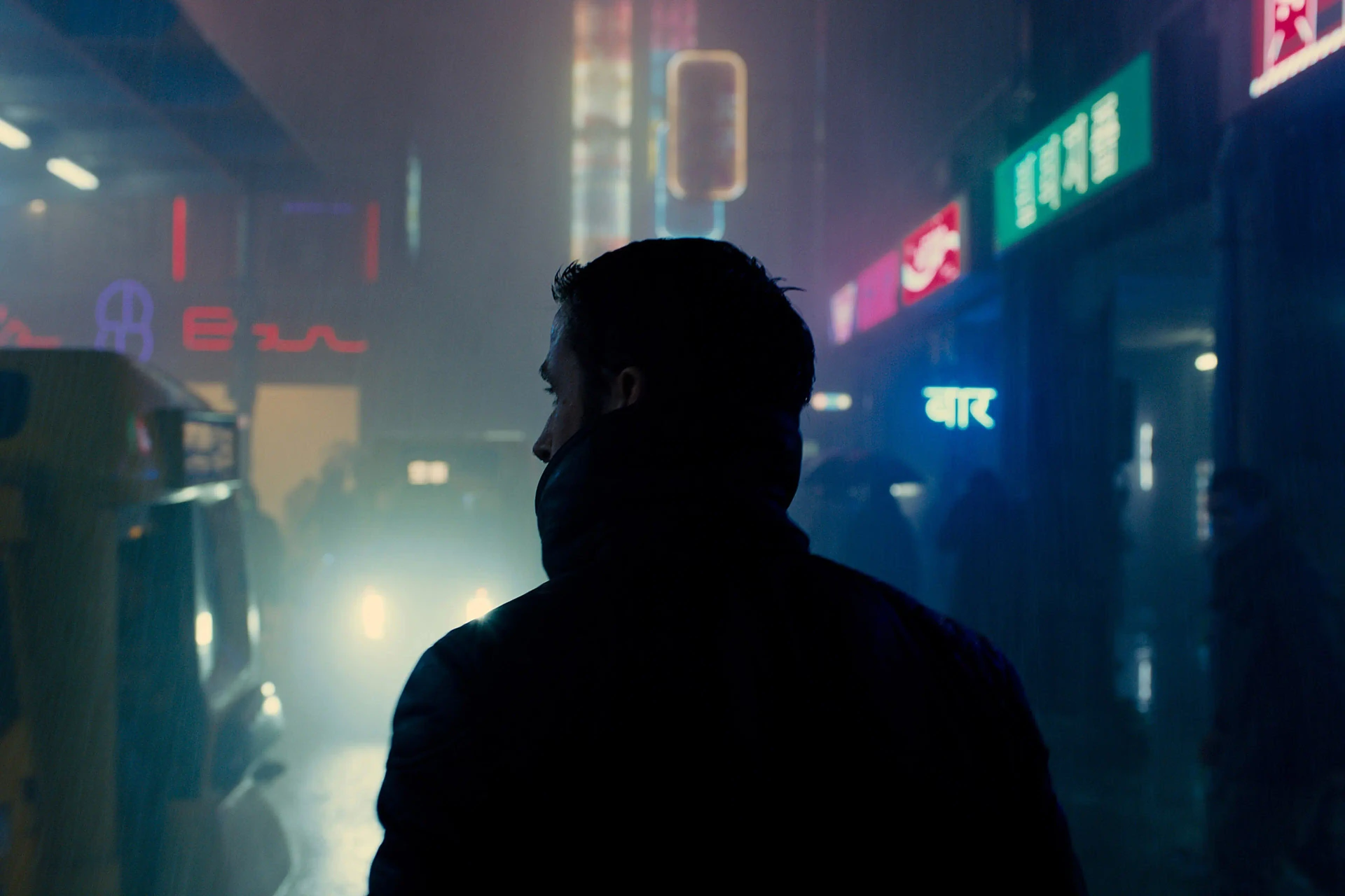 K stands in silhouette against a rain-soaked neon city in Blade Runner 2049.