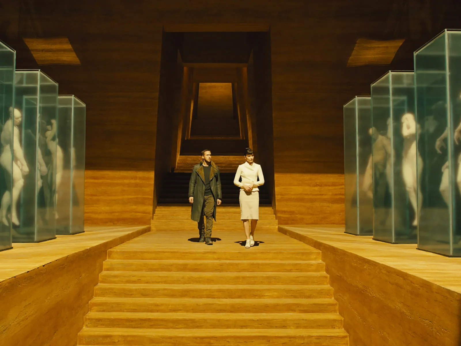 K walks beside Luv through the monumental amber interior of the Wallace Corporation.