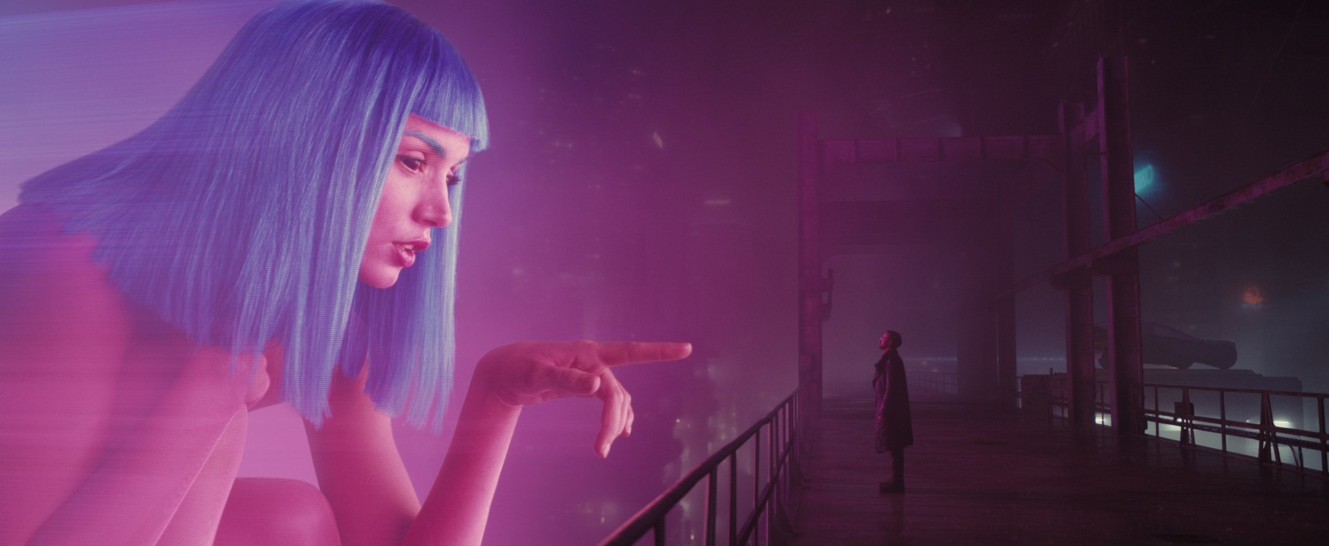 A giant holographic Joi advertisement reaches toward K in a dark purple cityscape.