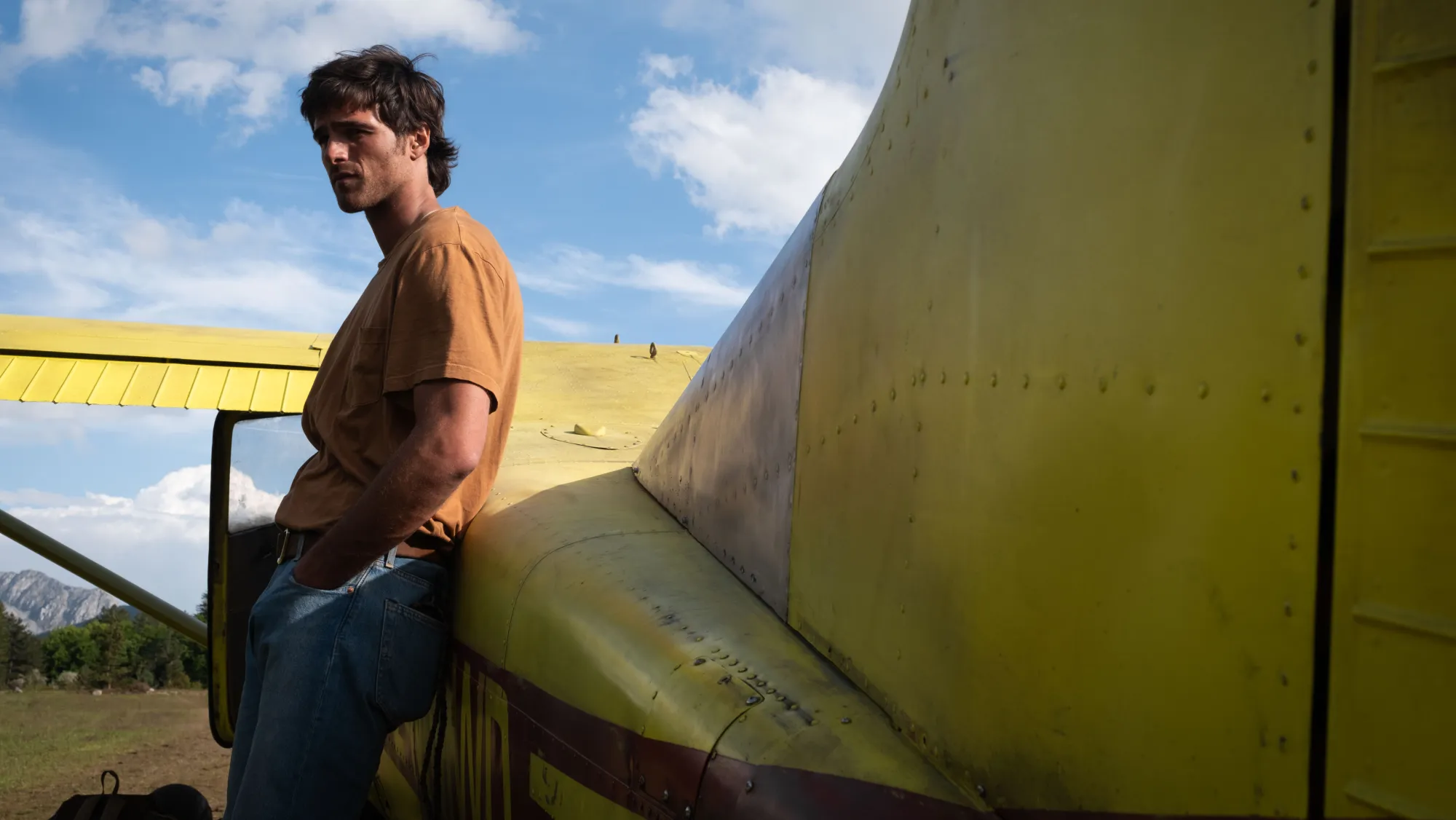 Jacob Elordi stands beside a yellow aircraft beneath a blue sky in The Dog Stars.