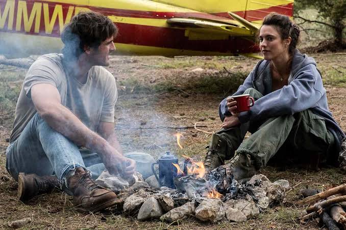 Jacob Elordi and Margaret Qualley sit beside a campfire near an aircraft in The Dog Stars.