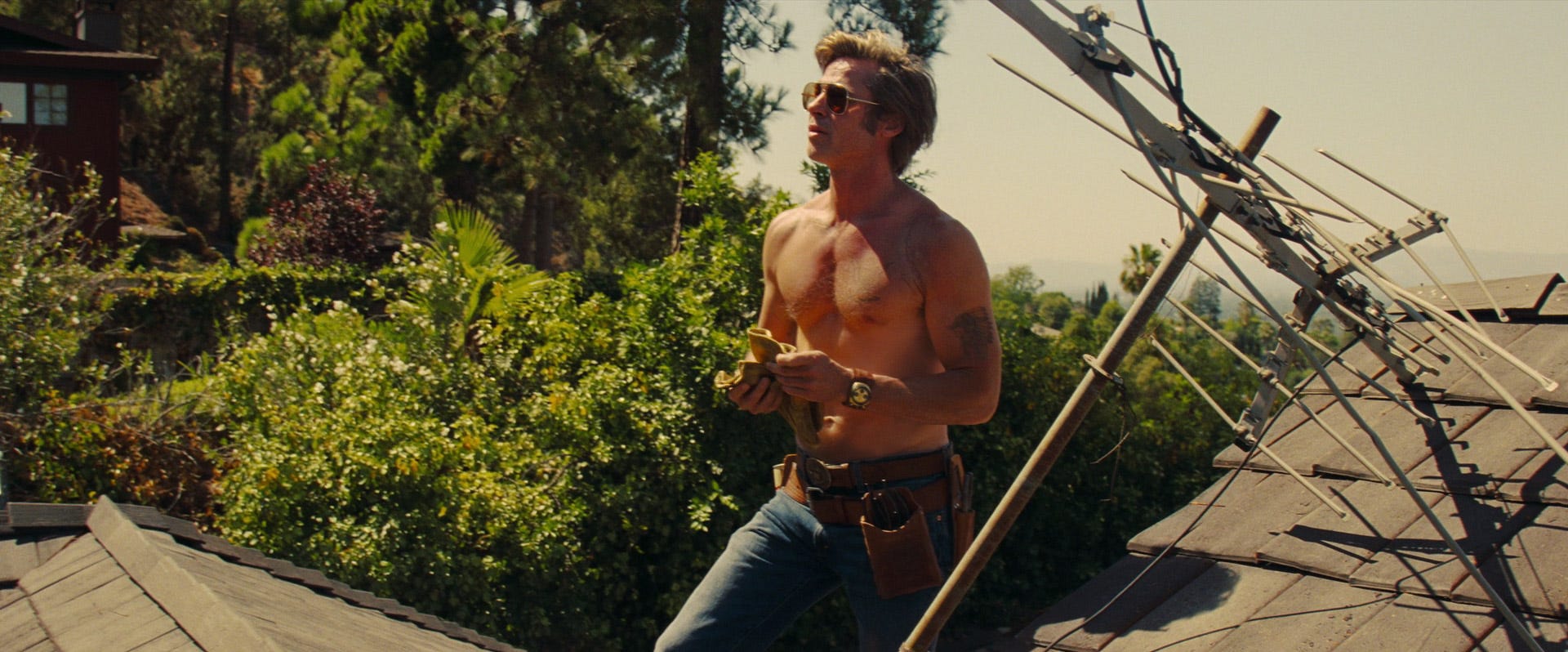Brad Pitt as Cliff Booth stands shirtless on a Los Angeles rooftop in Once Upon a Time… in Hollywood.