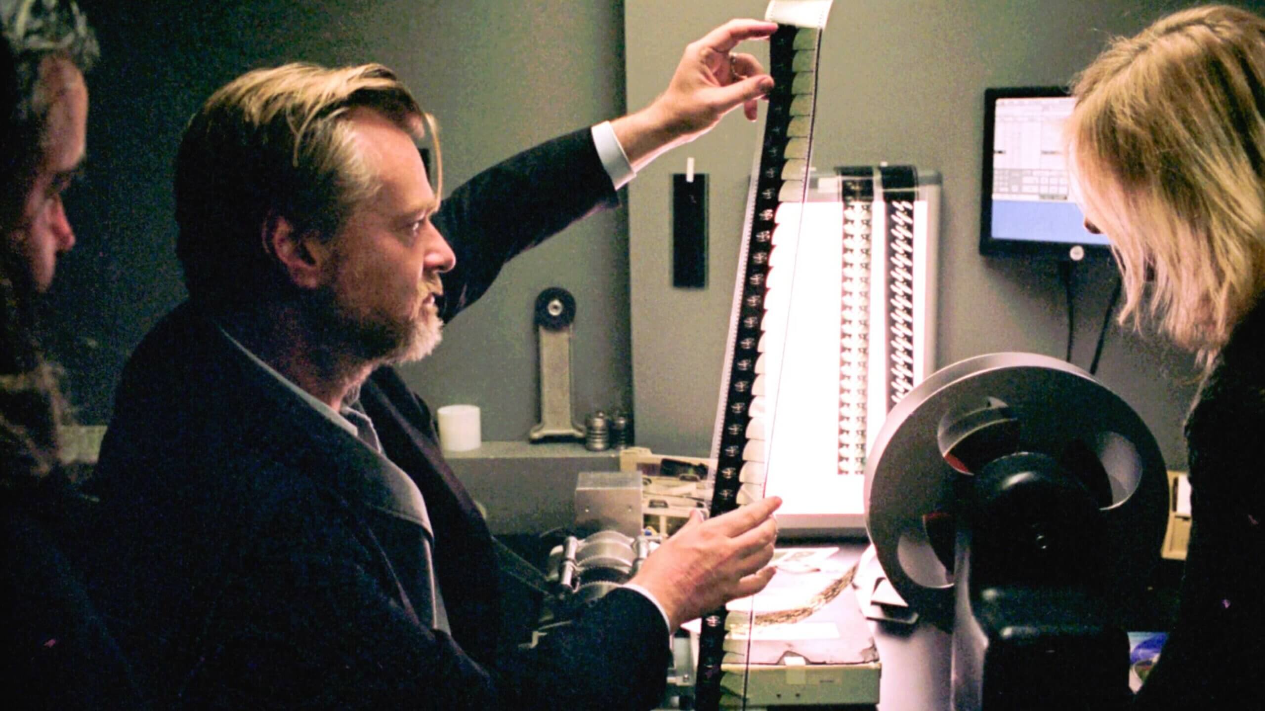 Christopher Nolan examines a strip of motion-picture film beside editing equipment.