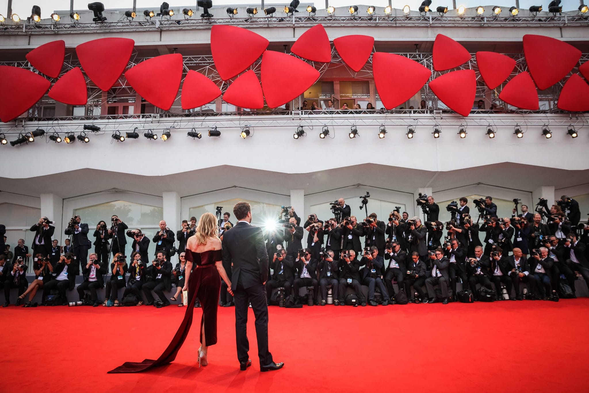 Guests stand on the red carpet facing a wall of photographers at the Venice Film Festival.