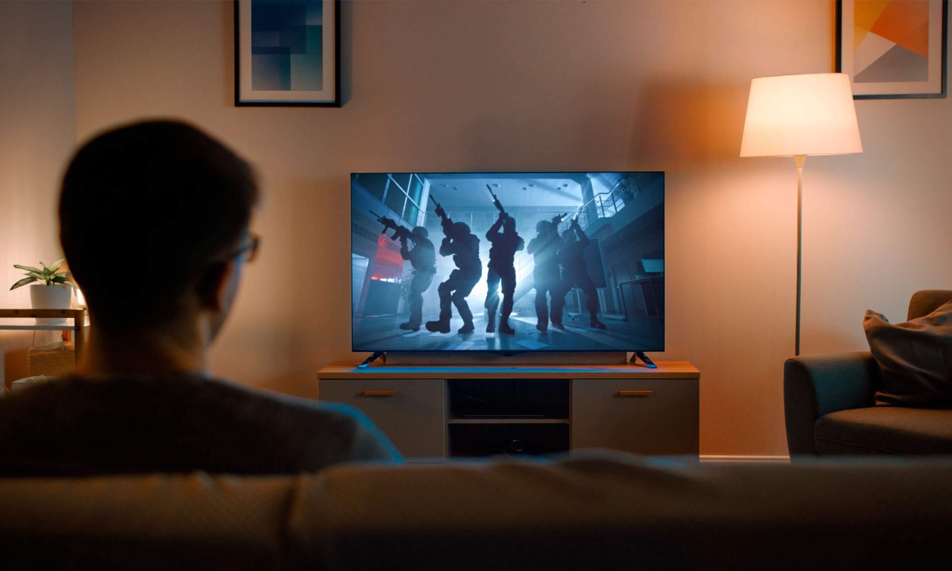 A person sits on a couch watching a movie on a television in a living room.