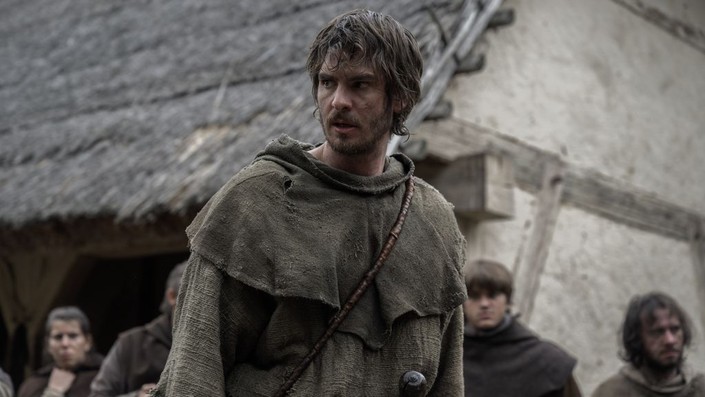 Andrew Garfield stands in a medieval village wearing rough brown clothing in The Uprising.