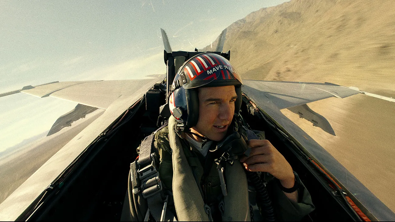 A fighter pilot sits in the cockpit of a jet flying through a mountainous landscape in Top Gun: Maverick.