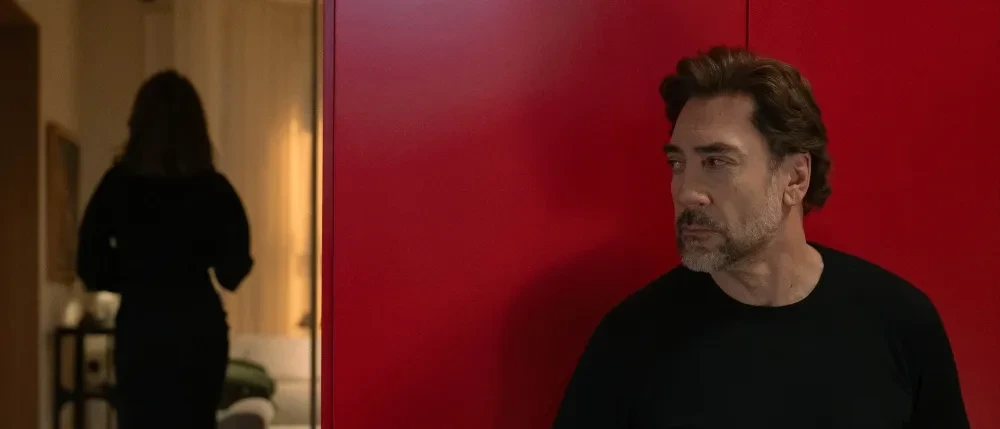 Javier Bardem stands against a vivid red wall inside a modern home