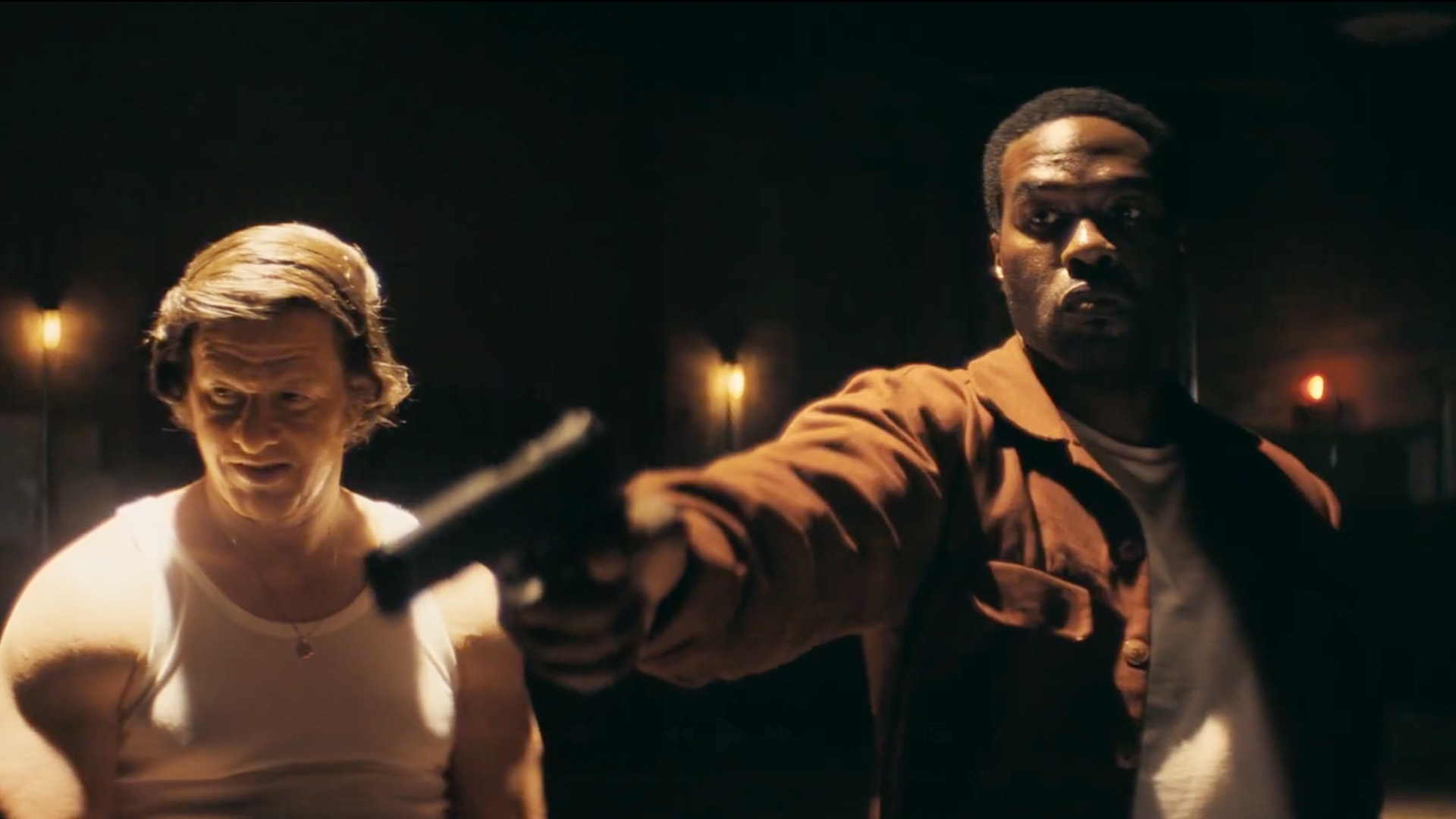 Mark Wahlberg and Yahya Abdul-Mateen II stand together in a dark room as Abdul-Mateen aims a handgun.