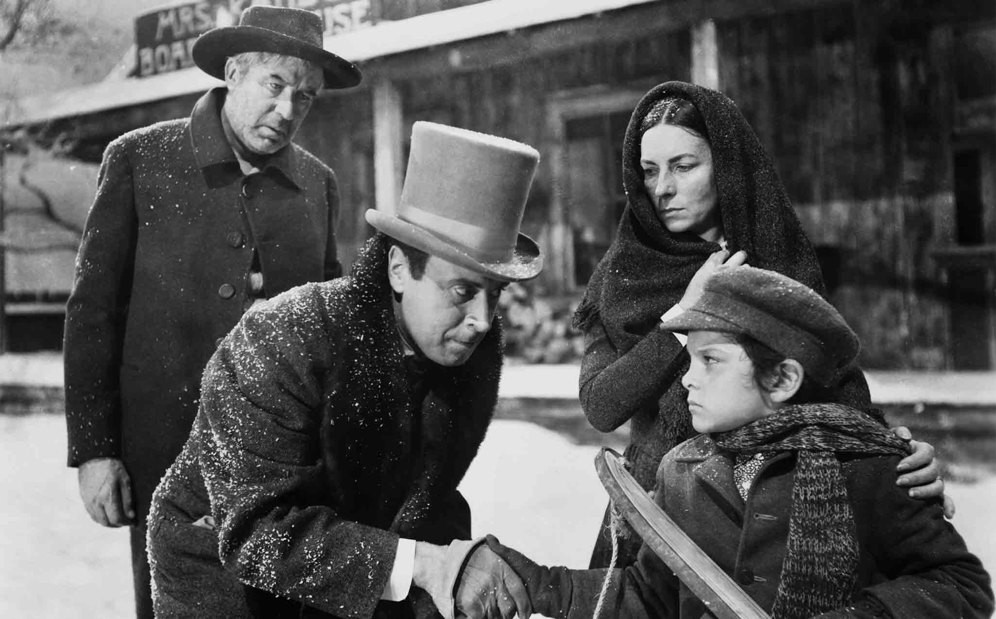 A young Charles Foster Kane stands in the snow while adults gather near him outside a boarding house.