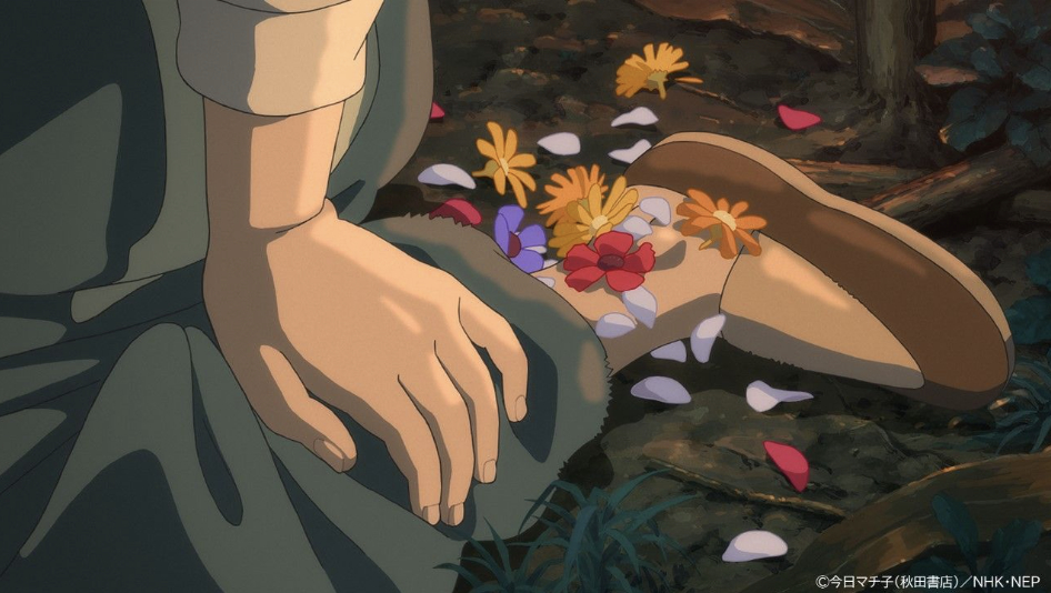 Flower petals rest inside and around a brown shoe beside a seated girl’s hand.