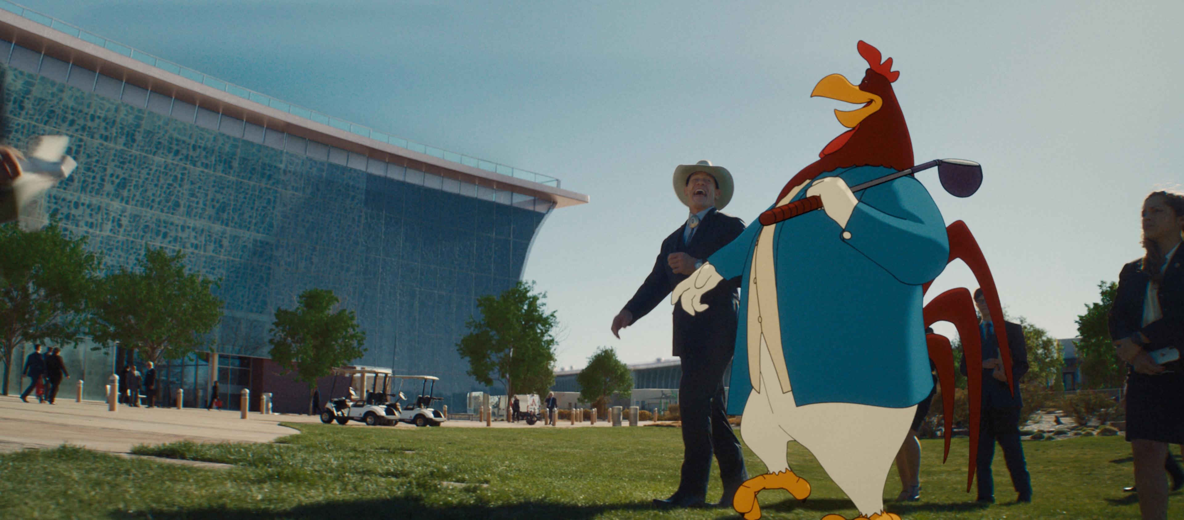 An animated Foghorn Leghorn stands on a lawn beside a live-action man outside a large corporate building in Coyote vs. Acme.