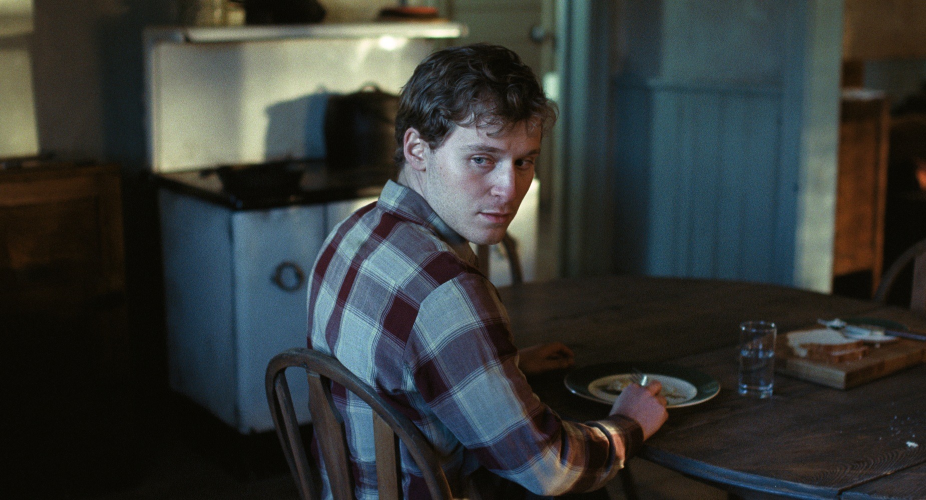 Andrew Scott sits at a wooden kitchen table and looks back over his shoulder.