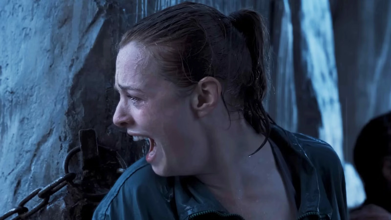 A soaked climber presses against an icy rock wall and shouts while trying to hold her position.