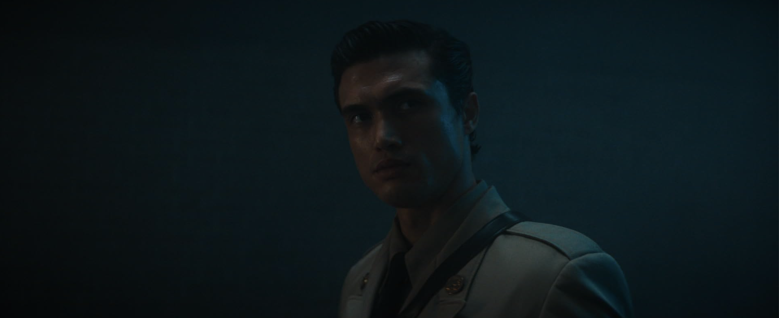 Charles Melton appears in a military uniform in a dark blue room.