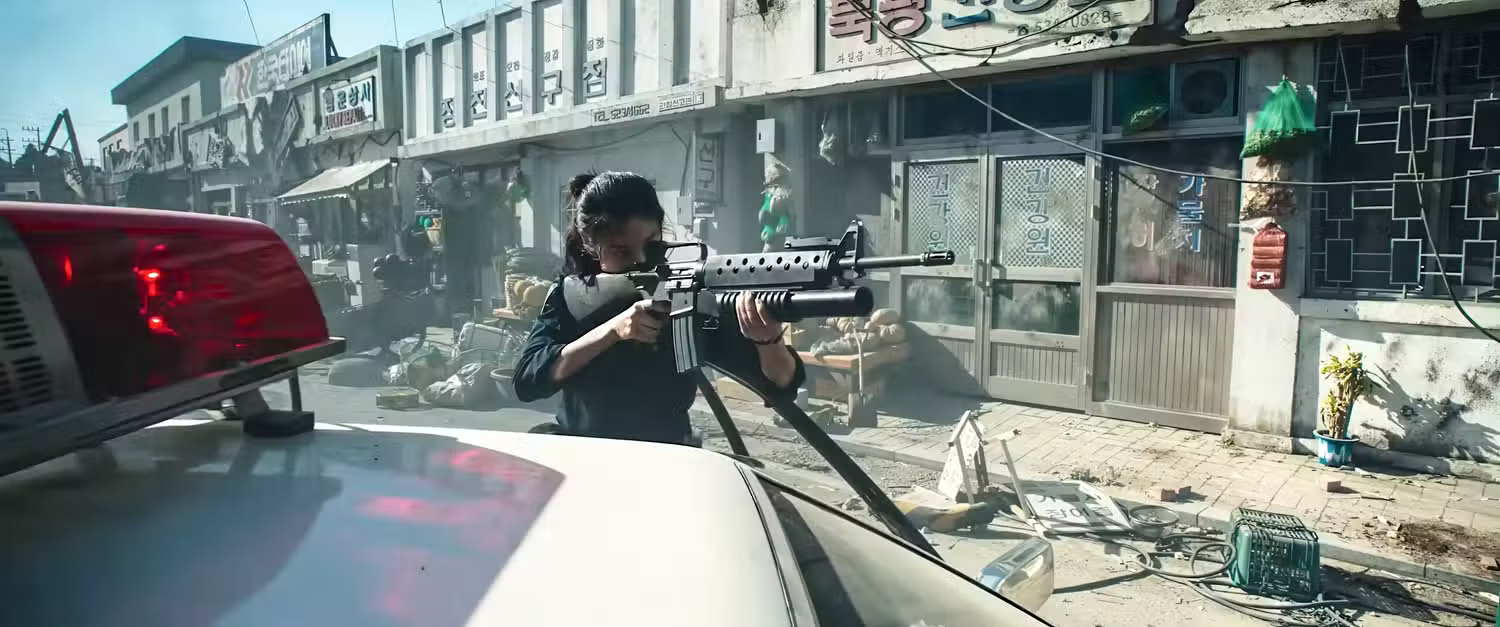 A woman aims a rifle from behind a police vehicle during a chaotic street battle in Hope.