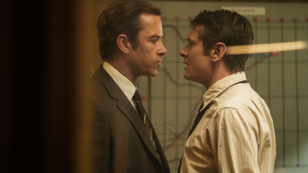 Guy Pearce and Jack O'Connell stand face to face inside a newspaper office