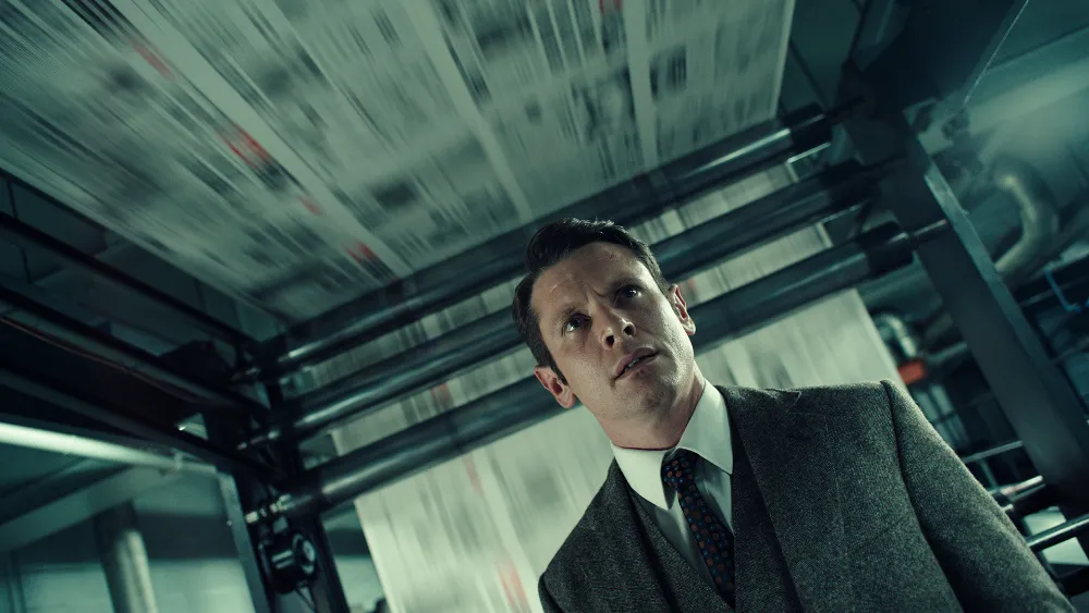 Jack O'Connell looks upward inside the machinery of a newspaper printing operation.