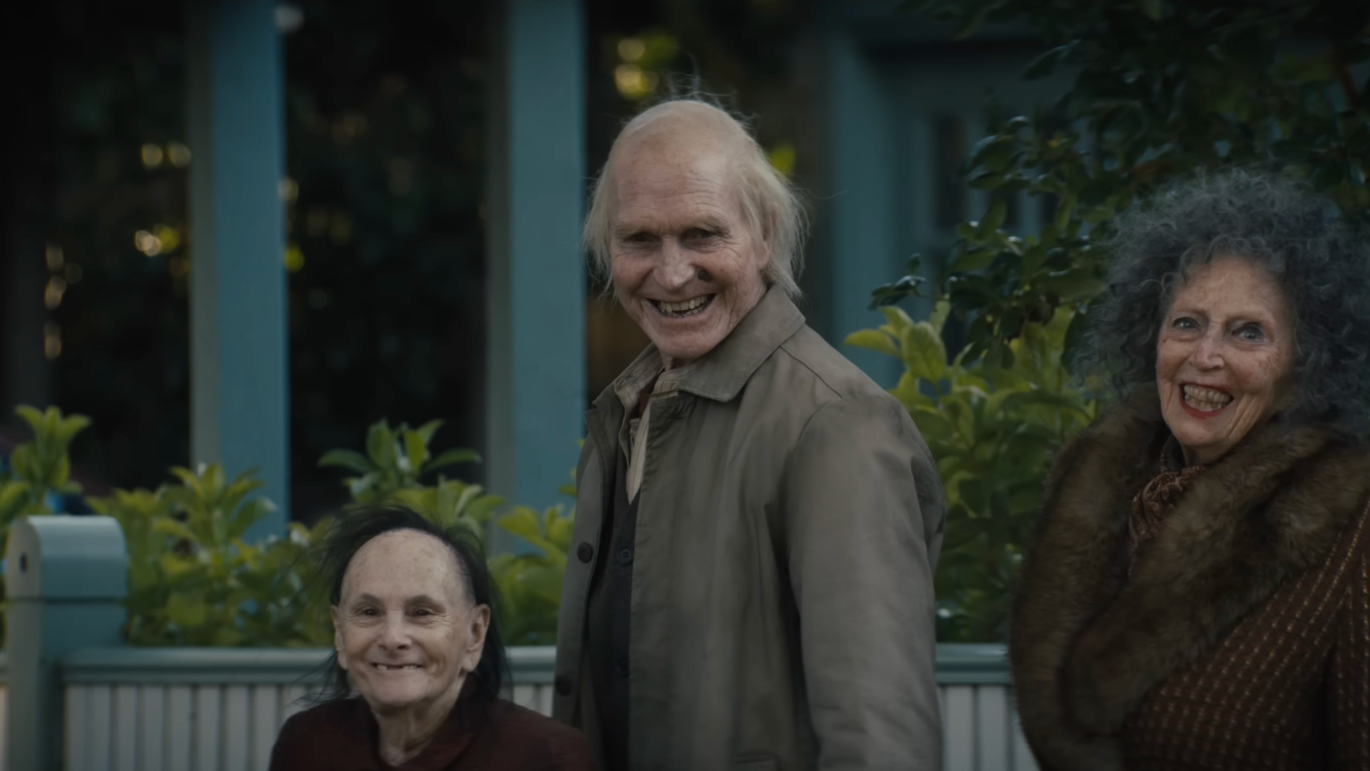 Three smiling elderly figures stand outside a house at dusk in Insidious: Out of the Further.
