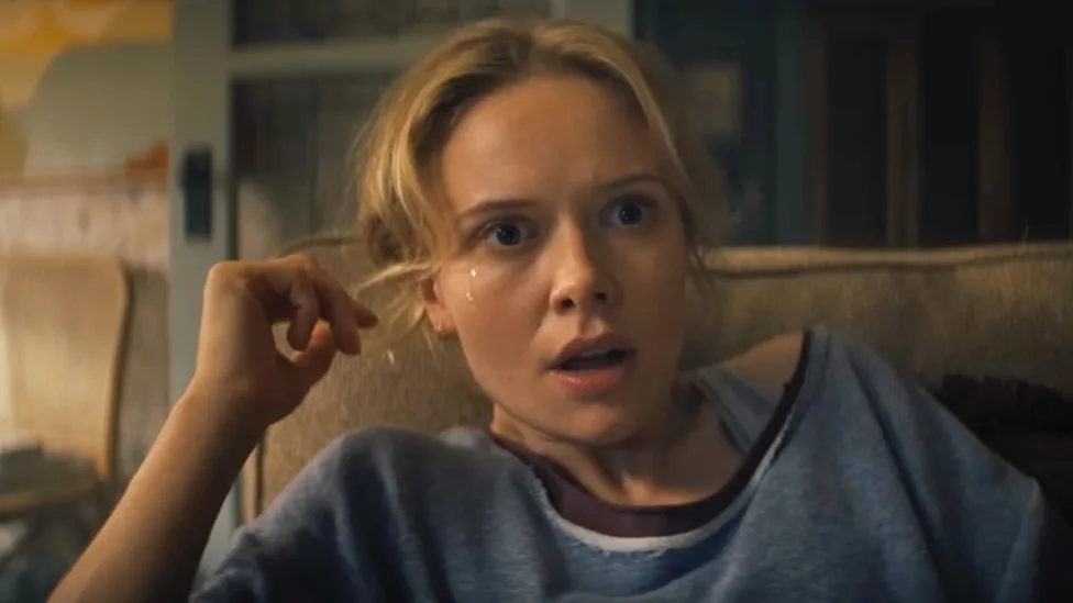 Amelia Eve as Gemma turns sharply toward something offscreen from a couch in Insidious: Out of the Further.