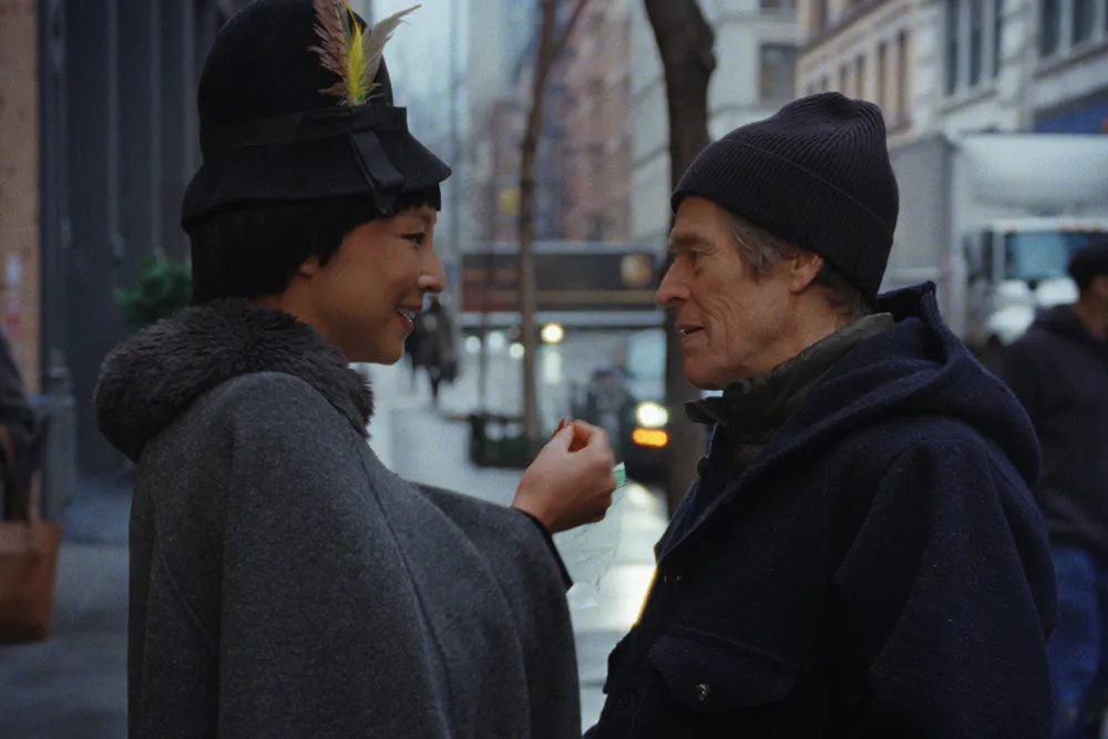 Two people in dark winter clothing stand facing each other on a city sidewalk.