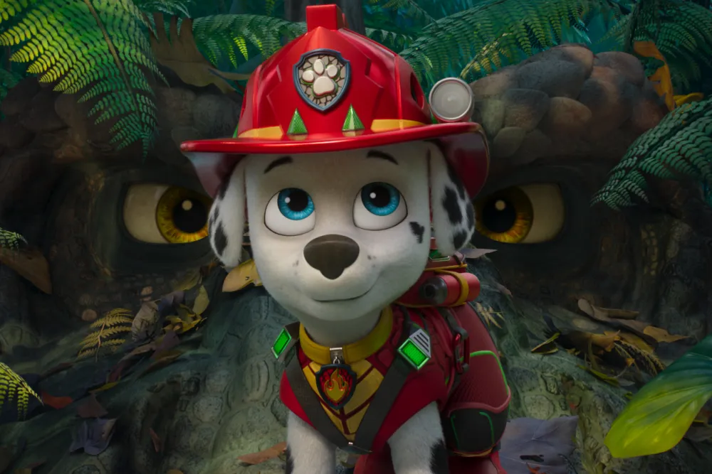 Marshall stands in firefighter gear while the eyes of a dinosaur appear behind him in PAW Patrol: The Dino Movie.