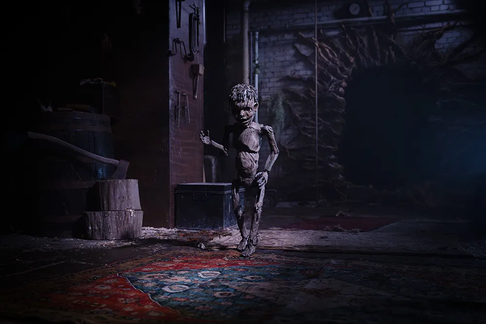 Pinocchio stands alone in a dark workshop surrounded by tools and wooden furniture.