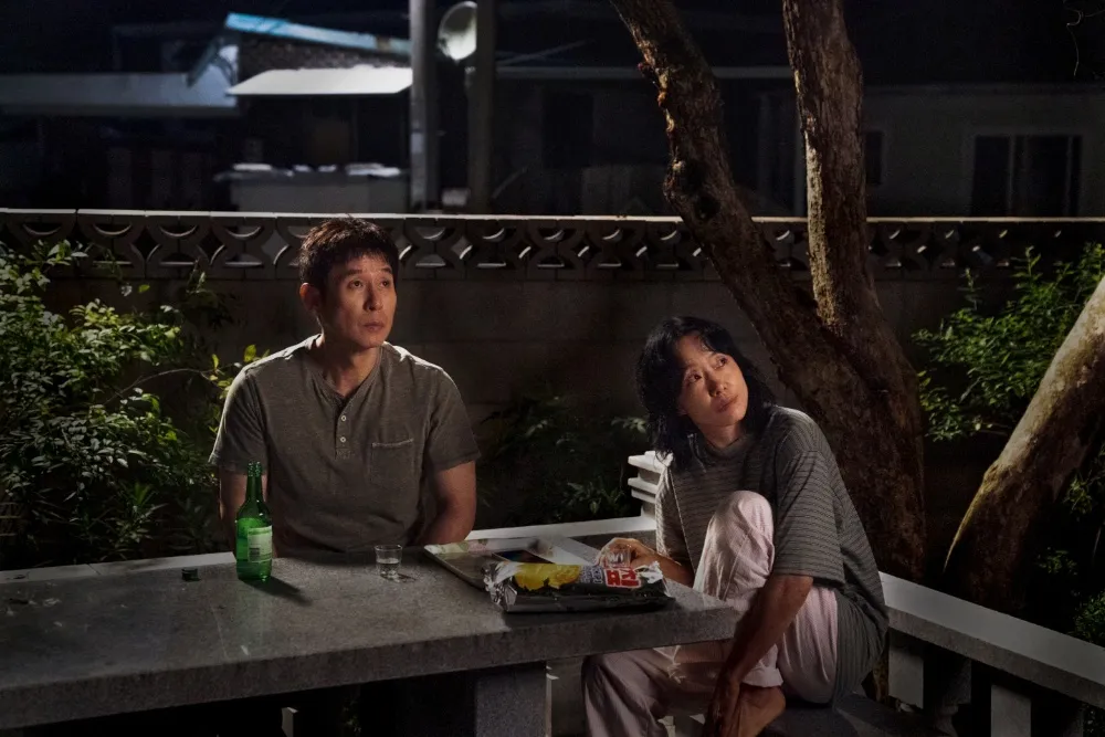 A man and woman sit together outside at night beside drinks and food.