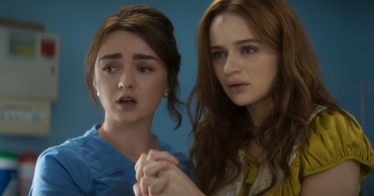 Maisie Williams and Joey King hold hands and look anxiously toward something outside the frame.