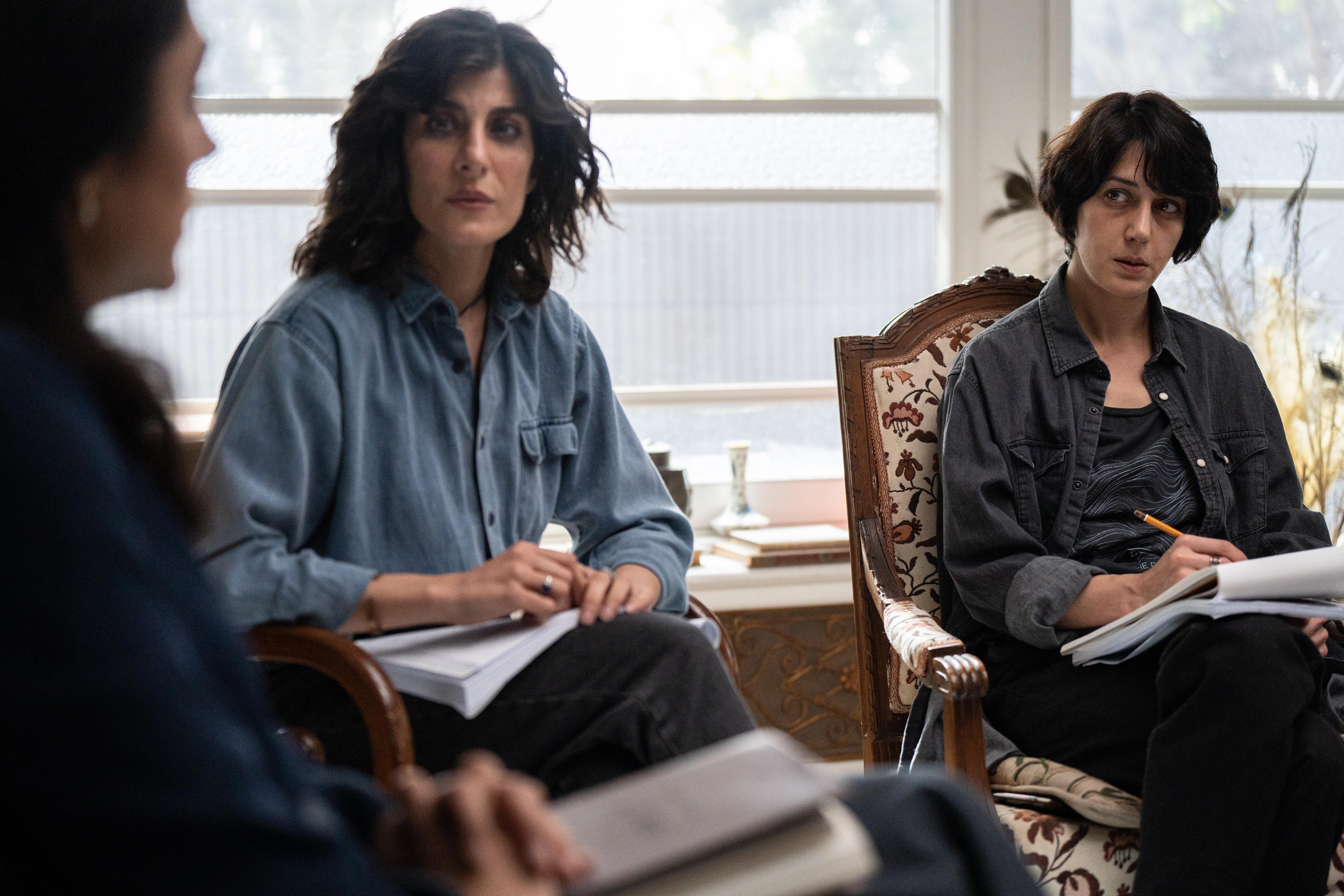 Golshifteh Farahani and another woman sit with notebooks during a discussion in a bright room.