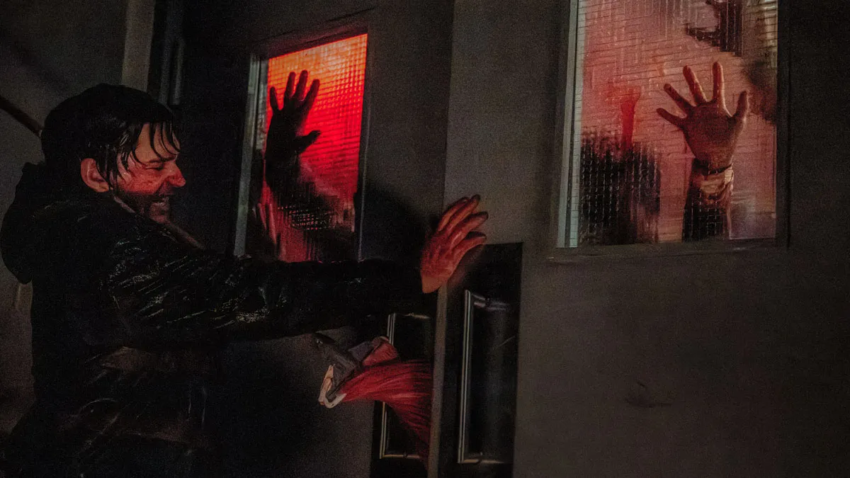 Austin Abrams braces near two windows glowing red as silhouetted hands press against the glass.