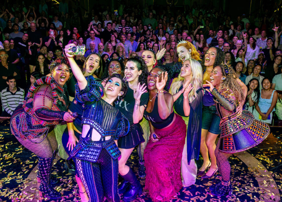 Members of the SIX cast pose for a photo with a cheering theater audience behind them.