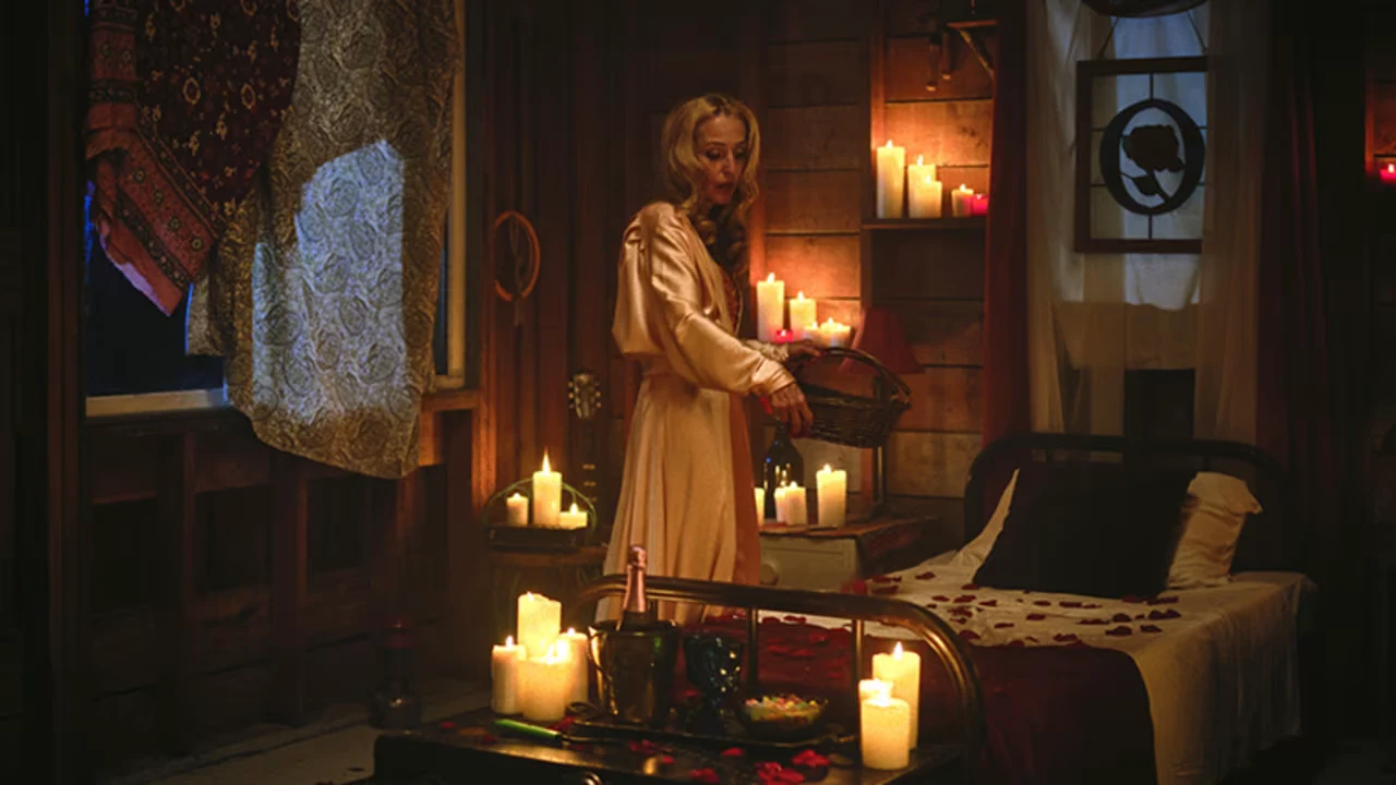 A woman in a pale robe stands inside a dark cabin illuminated by numerous candles.
