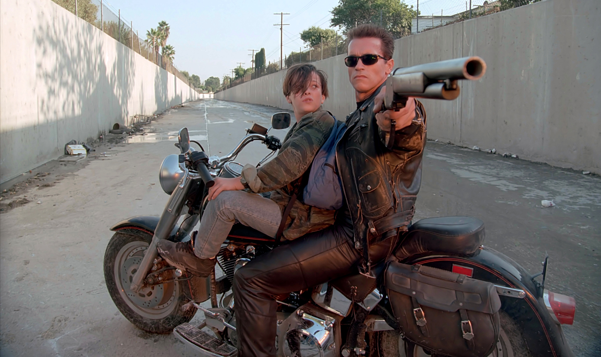 Arnold Schwarzenegger as the T-800 rides a motorcycle beside Edward Furlong as John Connor in Terminator 2: Judgment Day.