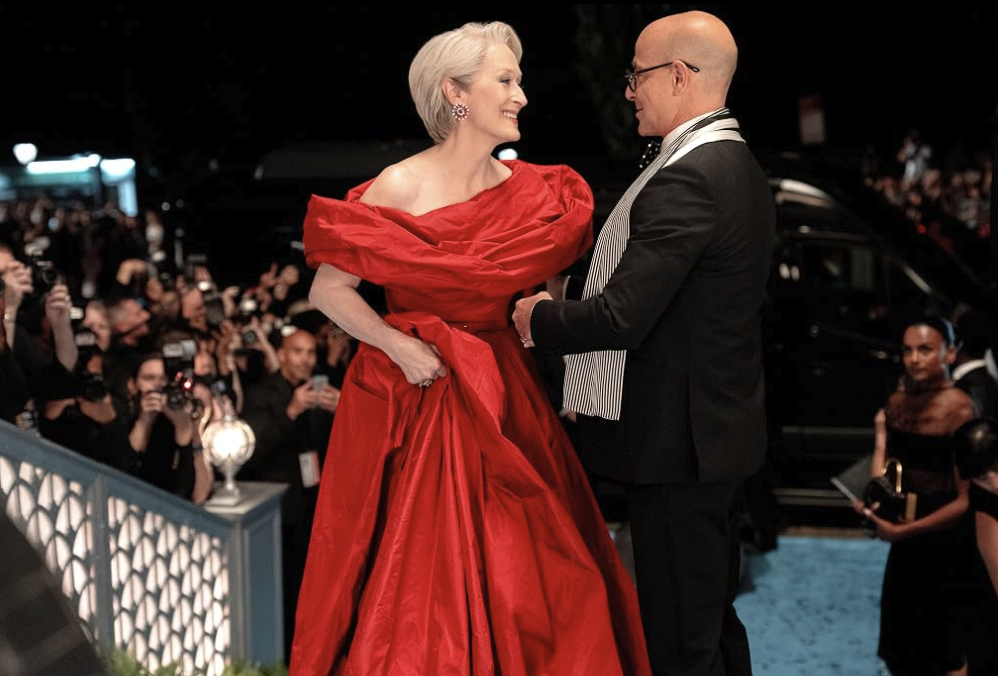 Meryl Streep in a red gown speaks with Stanley Tucci on a red carpet.